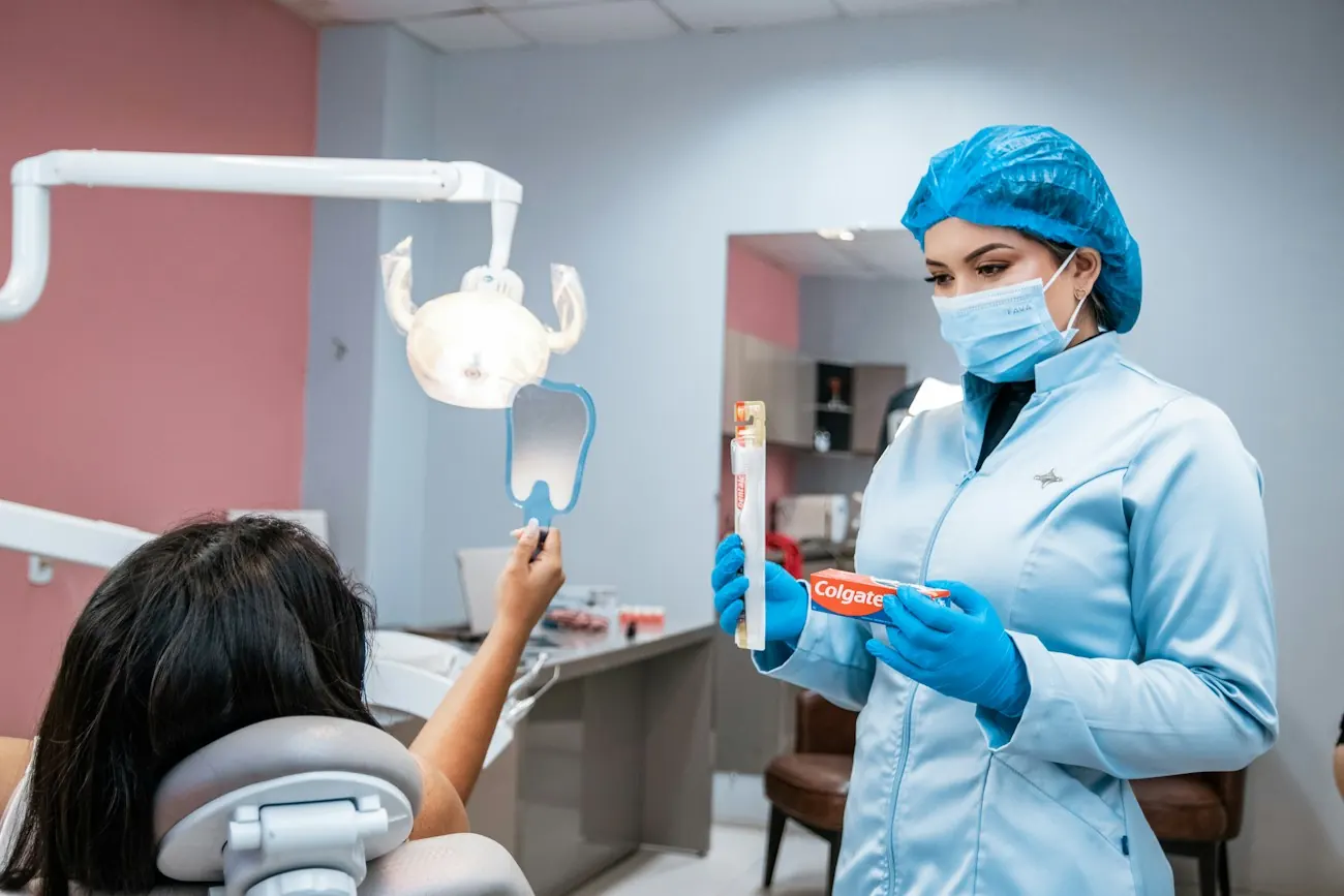 A dentist showing a girl in the chair how to brush her teeth